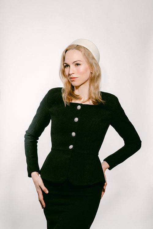 Woman wearing a black dress with white pillbox hat against a white background