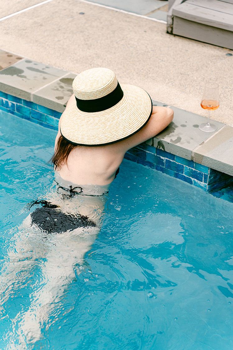 Person in a pool wearing a wide-brimmed hat and black bikini.