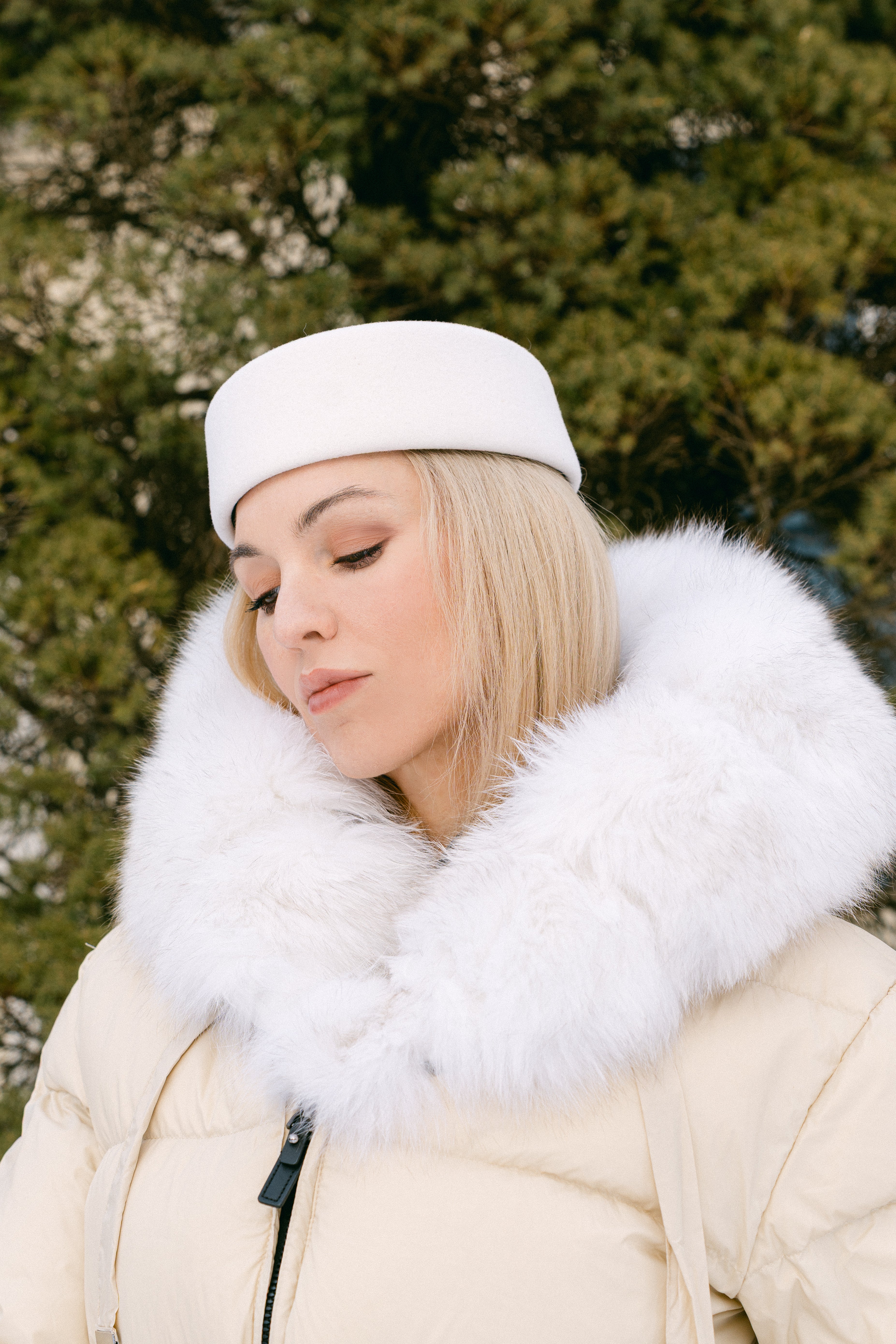 Woman wearing a white fur-lined coat and hat in front of a tree