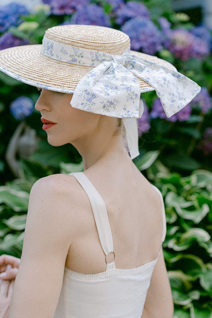 Woman wearing a wide-brimmed straw hat with a floral ribbon against a floral background