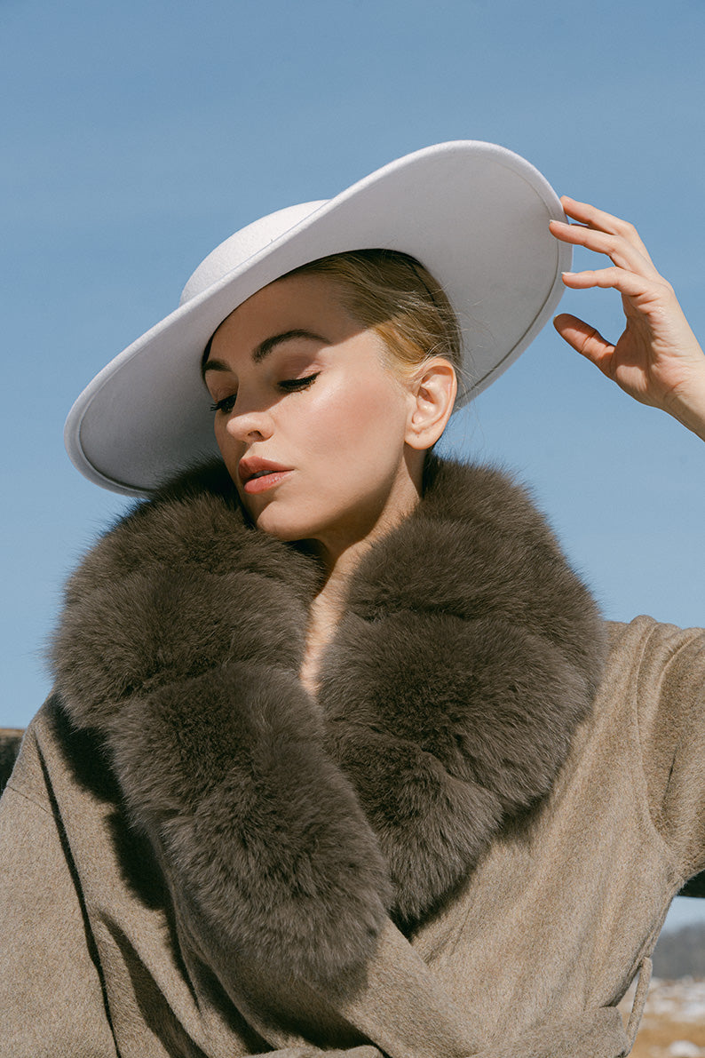 Person wearing a fur coat and white hat against a clear blue sky