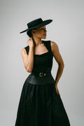 Woman wearing a black dress and hat against a gray background