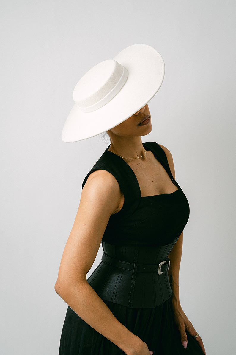 Woman wearing a black dress and white  wool brimmed hat against a gray background